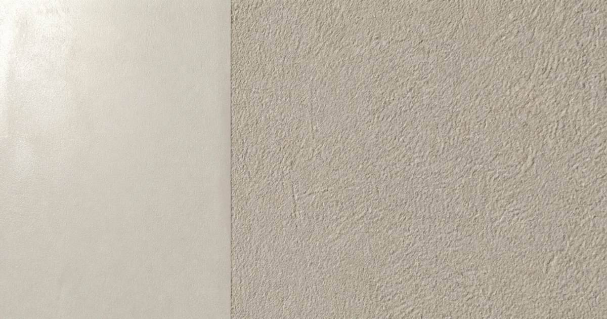Mur d'enduit clair où deux finitions du même matériau se rejoignent selon une arête verticale nette, l'une lisse et satinée, l'autre au grain marqué.